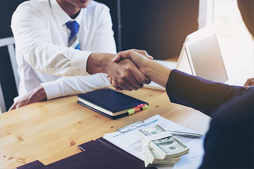 male and female shaking hands over a stack of cash