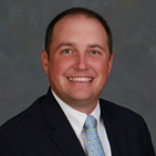 Professional headshot of Matthew Hess wearing a black jacket over a white shirt and light blue tie.